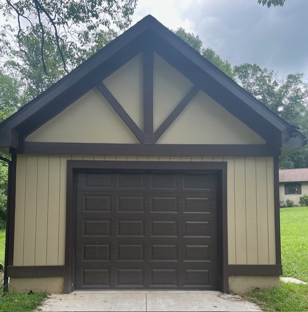 Detached garage with a brown garage door and light-colored siding. Surrounded by greenery, it reflects a classic architectural style.