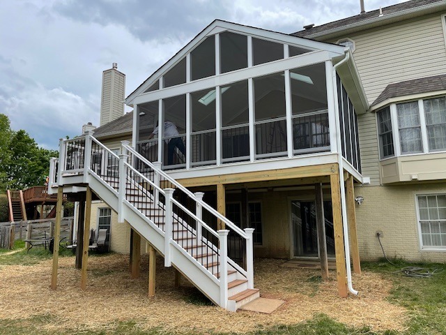 Newly constructed screened porch with a staircase, elevated above the backyard. Features include large windows and a sturdy wooden framework, enhancing outdoor living space.